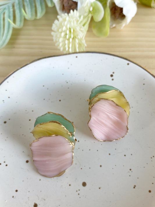 Pendientes de arcilla polimérica de la colección Pétalos en tonos rosa, amarillo y verde menta, con formas orgánicas superpuestas y bordes dorados.